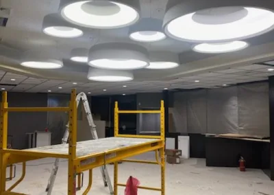 Interior of a construction site with scaffolding and a ladder under circular lights in the ceiling, debris scattered on the floor.